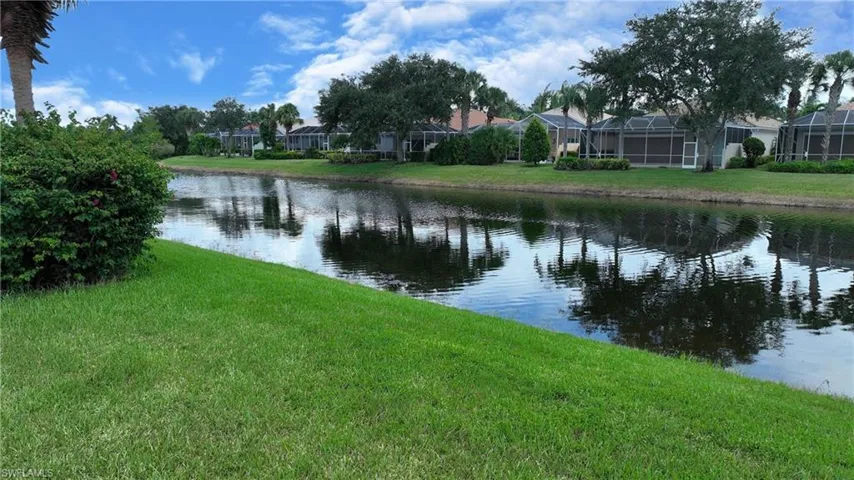 Waterfront property featuring a landscaped canal, lush green lawn, mature trees, and screened enclosures