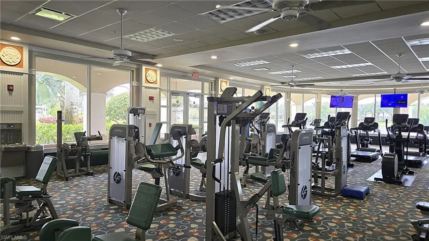 Fitness center with diverse exercise equipment, large windows, ceiling fans, and integrated wall-mounted screens
