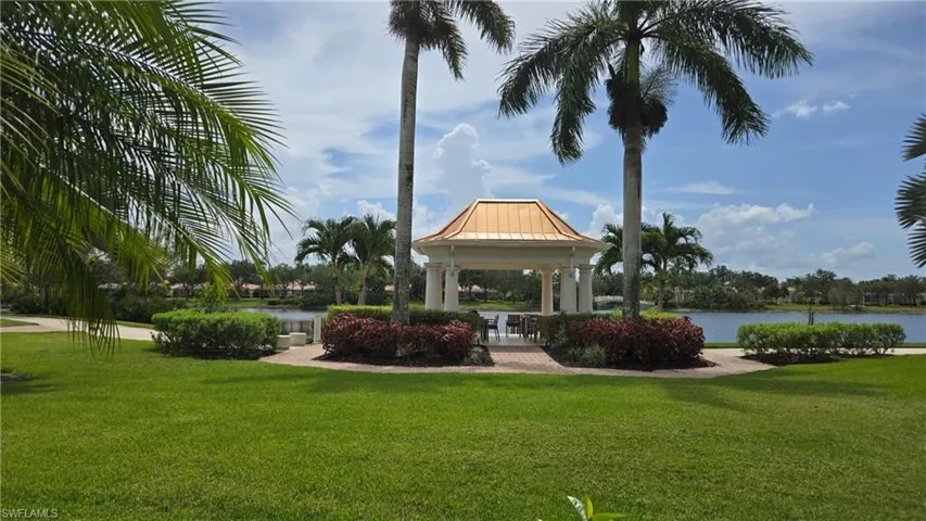 Lakeside gazebo with a domed roof and column supports, surrounded by manicured landscaping, mature palm trees, and a paved walkway