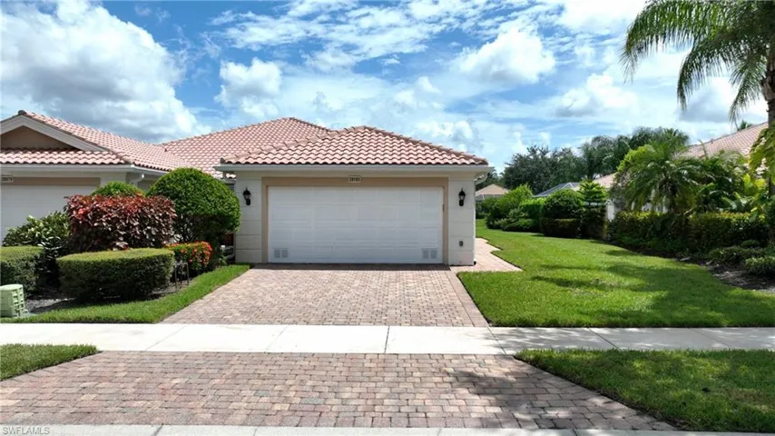 Terracotta tile roof with a prominent garage, a paver driveway, and mature landscaping