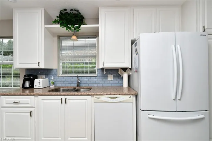 White shaker-style cabinetry, double-basin stainless steel sink, light blue subway tile backsplash, laminate countertops, and built-in dishwasher