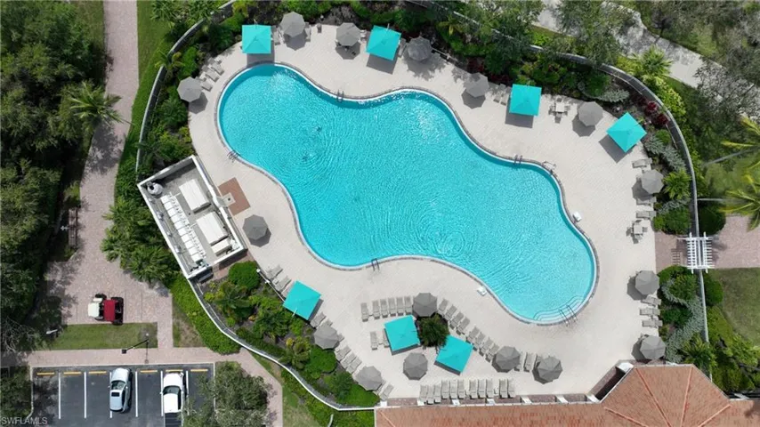 Freeform swimming pool with integrated seating, surrounded by a paved deck, multiple shade umbrellas, and various lounge chairs