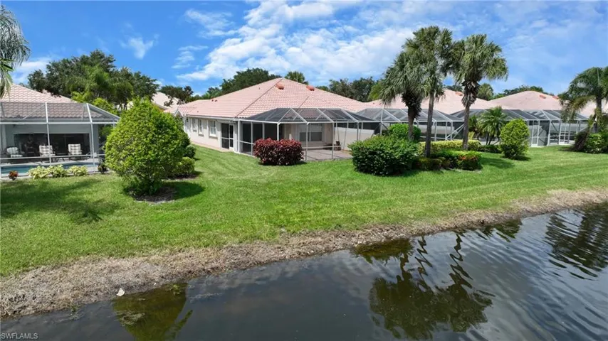 Waterfront property featuring multiple screened enclosures, mature palm trees, and lush green landscaping