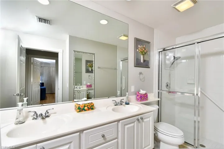 Dual vanity with white cabinetry, a large wall-mounted mirror, and a glass-enclosed shower with a sliding door