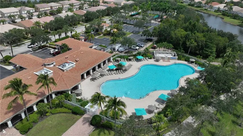 L-shaped structure with a tile roof, an irregularly shaped swimming pool, surrounding lounge seating, and mature palm trees