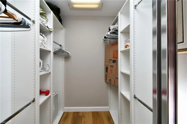 Walk-in closet with integrated white shelving, chrome hanging rods, and wood-finish flooring