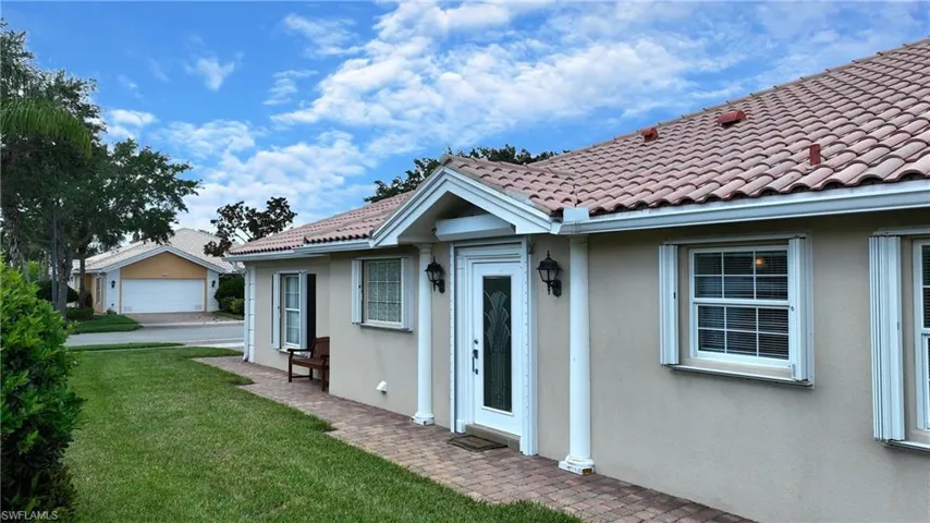 Neutral-toned stucco exterior with a terra cotta tile roof, front entry with decorative glass, and a brick paver walkway