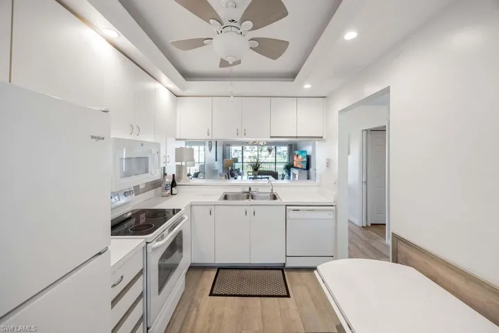Kitchen featuring white cabinetry, light hardwood / wood-style floors, sink, white appliances, and a raised ceiling