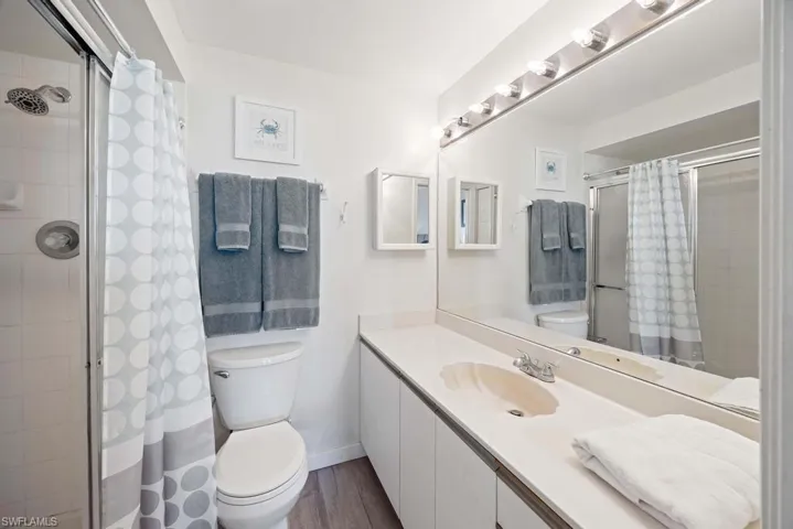 Bathroom with a tile shower, vanity, toilet, and wood-type flooring