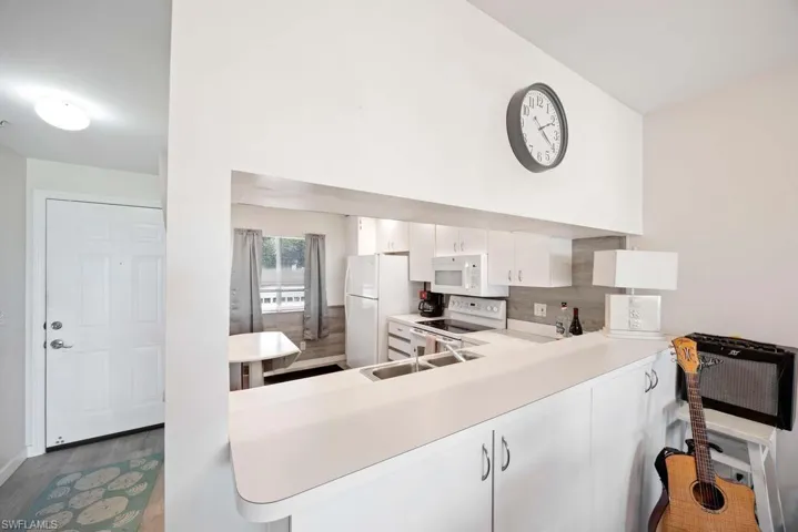 Kitchen with white cabinetry, kitchen peninsula, hardwood / wood-style flooring, sink, and white appliances