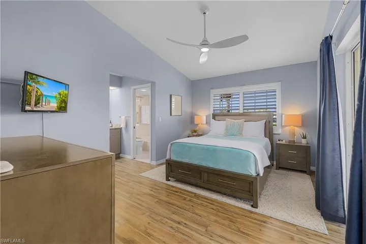 Bedroom with vaulted ceiling, light wood-style flooring, a ceiling fan, and ensuite bathroom