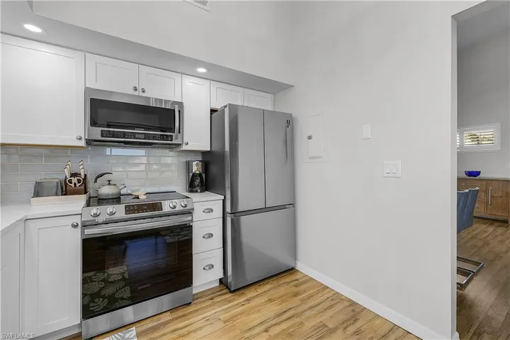 Kitchen featuring stainless steel appliances, white cabinets, light wood-style floors, decorative backsplash, and a high ceiling