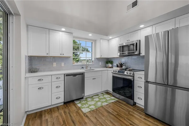 Kitchen featuring stainless steel appliances, white cabinetry, dark wood-type flooring, recessed lighting, and tasteful backsplash