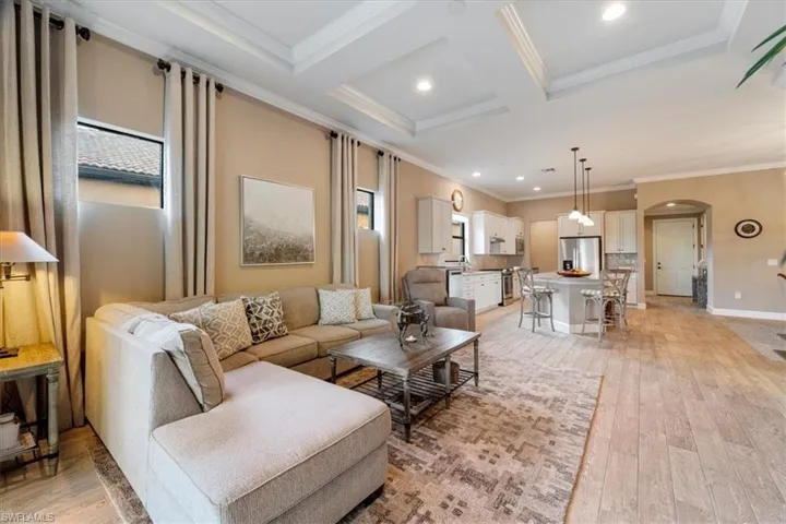 Living room featuring arched walkways, light wood-style flooring, ornamental molding, recessed lighting, and coffered ceiling