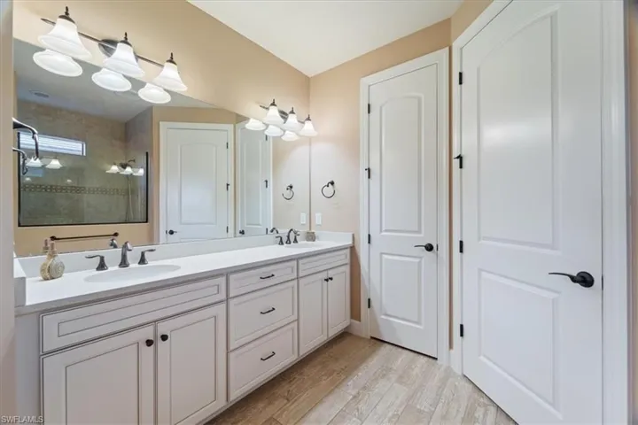 Bathroom featuring double vanity, walk in shower, and light wood-style floors