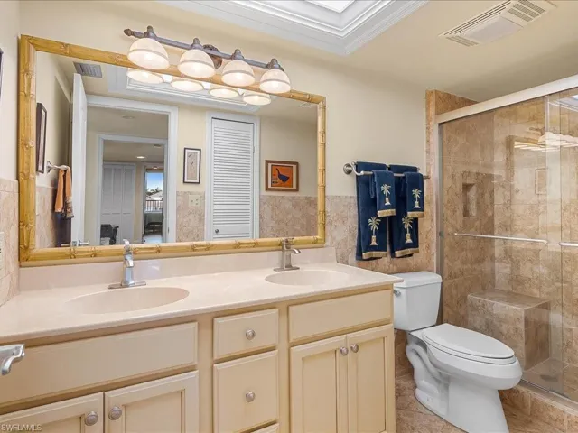 Full primary en suite bathroom featuring double vanity, tile walls, a shower stall, ornamental molding, and light tile patterned flooring