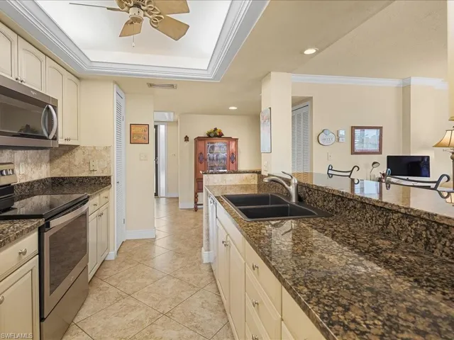 Kitchen with appliances with stainless steel finishes, crown molding, dark stone countertops, ceiling fan, and backsplash