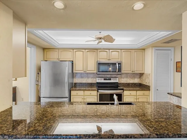 Kitchen with a tray ceiling, appliances with stainless steel finishes, a peninsula, and dark stone counters