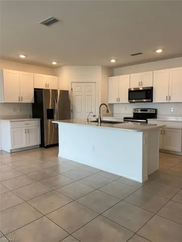Kitchen featuring recessed lighting, white cabinets, stainless steel appliances, light tile patterned floors, and a center island with sink