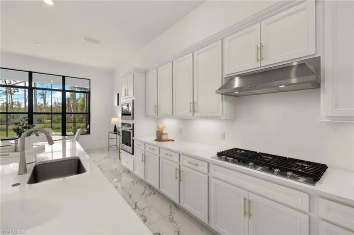 Kitchen featuring a sink, light countertops, under cabinet range hood, appliances with stainless steel finishes, and white cabinets