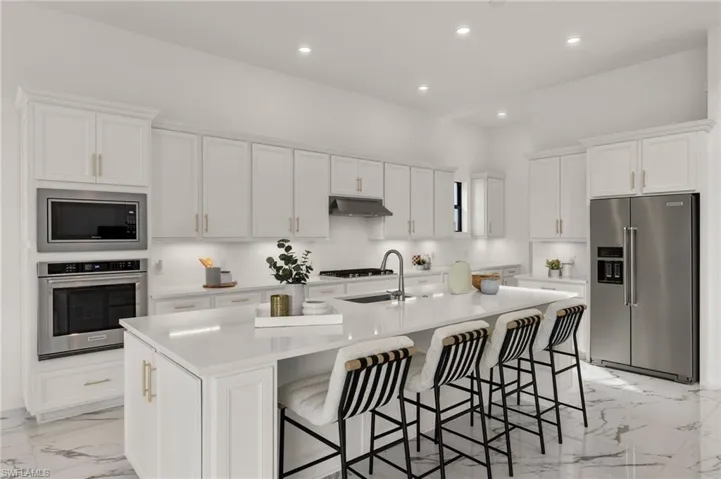 Kitchen with light countertops, a kitchen island with sink, under cabinet range hood, stainless steel appliances, and white cabinets