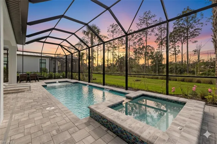 Pool at dusk featuring a sunroom, a pool with connected hot tub, a patio area, a yard, and a lanai