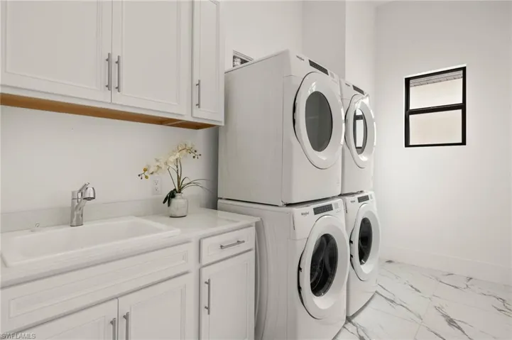 Clothes washing area with marble finish floor, stacked washer and dryer, cabinet space, baseboards, and a sink