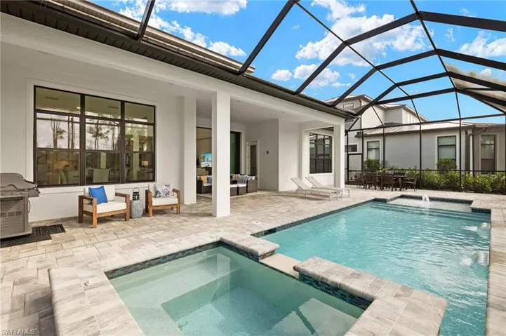View of pool featuring a pool with connected hot tub, grilling area, glass enclosure, a patio, and outdoor lounge area