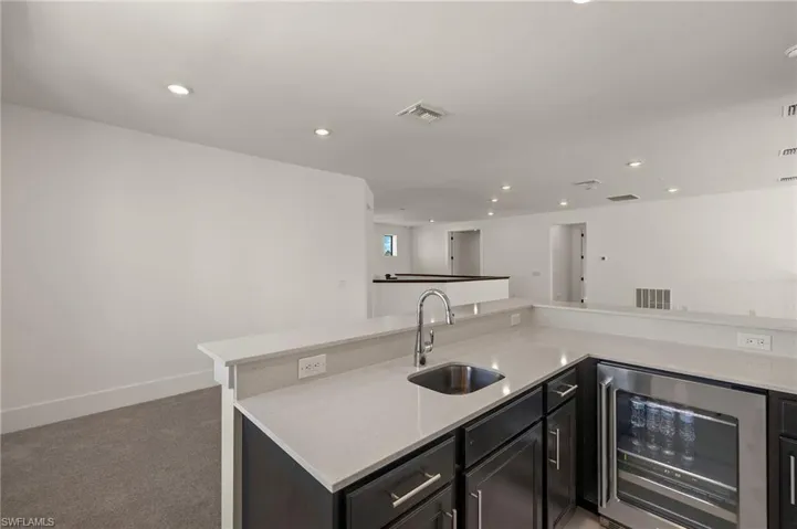 Kitchen with carpet, beverage cooler, visible vents, and a sink