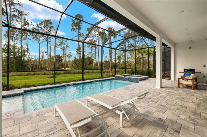 View of swimming pool featuring a lanai, a patio, a lawn, and a pool with connected hot tub