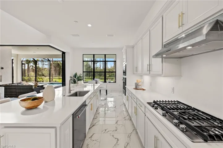 Kitchen with marble finish floor, a sink, light countertops, under cabinet range hood, and appliances with stainless steel finishes