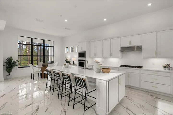 Kitchen with a center island with sink, light countertops, stainless steel appliances, white cabinetry, and under cabinet range hood