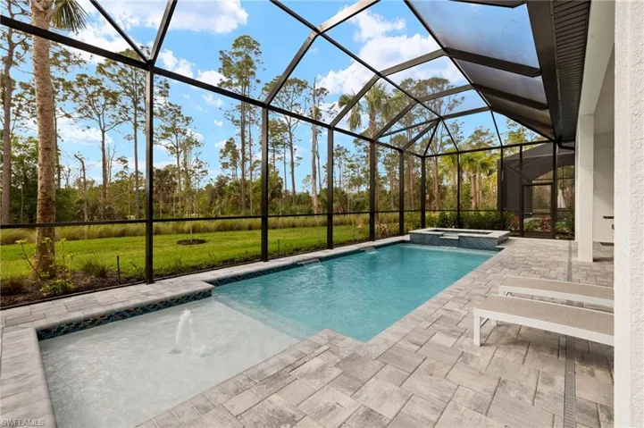 View of swimming pool with a patio, glass enclosure, and a pool with connected hot tub