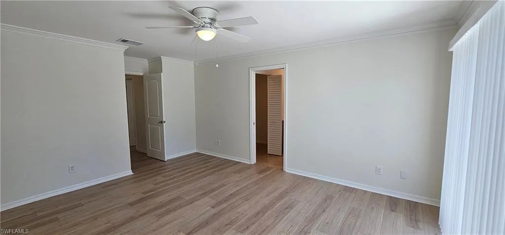 Unfurnished bedroom with ornamental molding, light wood-type flooring, a ceiling fan, and a walk in closet