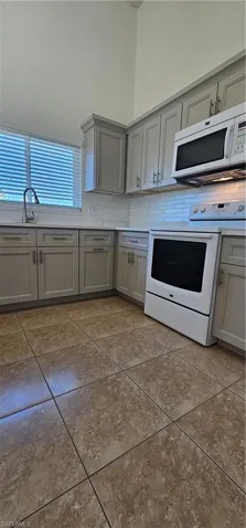 Kitchen featuring gray cabinets, range, backsplash, and light countertops