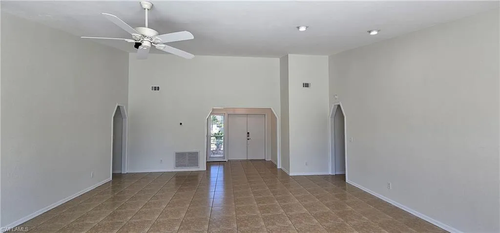 Unfurnished living room with arched walkways, a high ceiling, a ceiling fan, and light tile patterned flooring