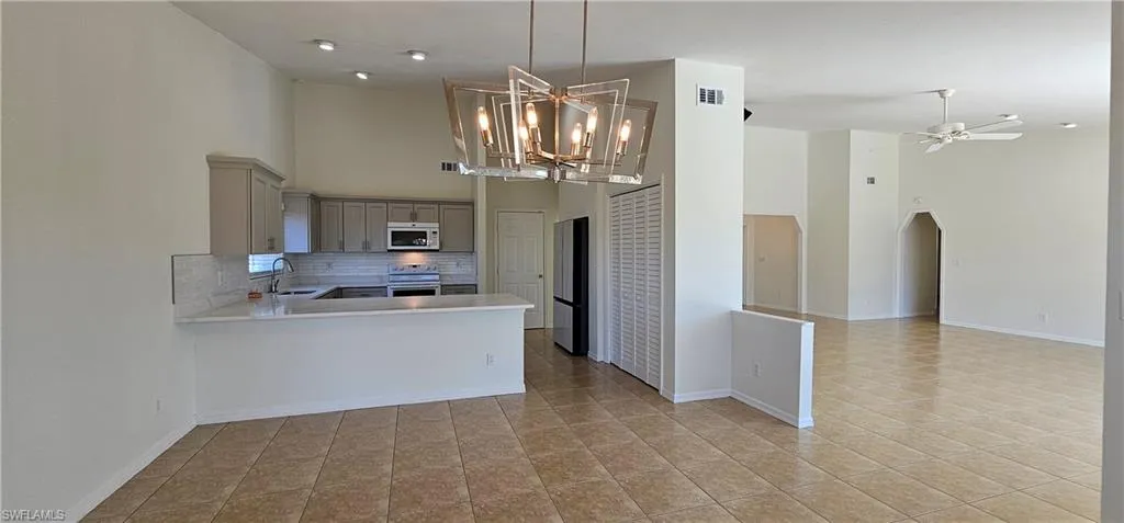 Kitchen with gray cabinetry, a high ceiling, tasteful backsplash, arched walkways, and open floor plan