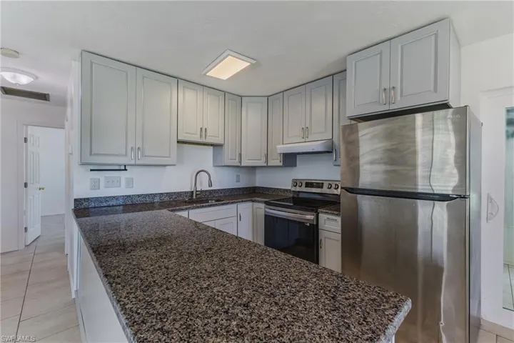 Kitchen featuring stainless steel appliances, dark stone countertops, light tile patterned floors, and a peninsula