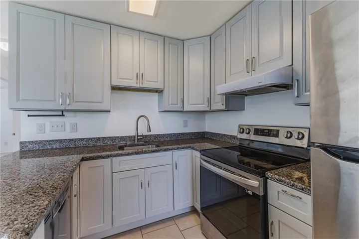 Kitchen with stainless steel appliances, dark stone countertops, and light tile patterned floors
