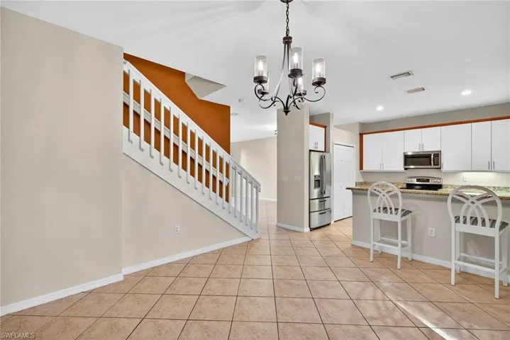 Kitchen featuring a kitchen bar, white cabinets, stainless steel appliances, a chandelier, and light stone counters