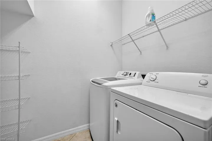 Laundry area with separate washer and dryer, light tile patterned floors, and a textured wall