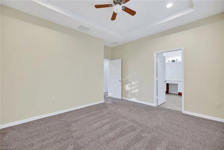 Unfurnished bedroom with built in study area, a raised ceiling, carpet floors, ceiling fan, and connected bathroom