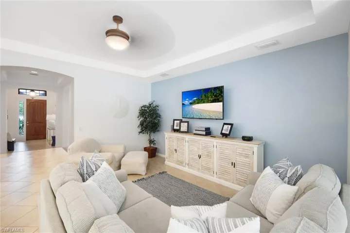 Living room featuring a raised ceiling, light tile patterned floors, and ceiling fan.