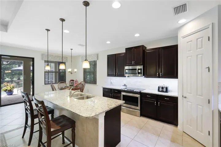 Kitchen featuring decorative light fixtures, tasteful backsplash, an island with sink, a breakfast bar area, and appliances with stainless steel finishes