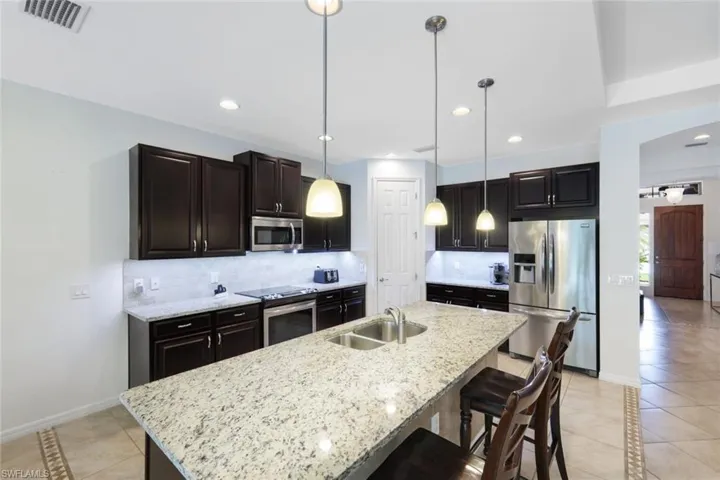 Kitchen featuring decorative light fixtures, decorative backsplash, an island with sink, a breakfast bar area, and appliances with stainless steel finishes