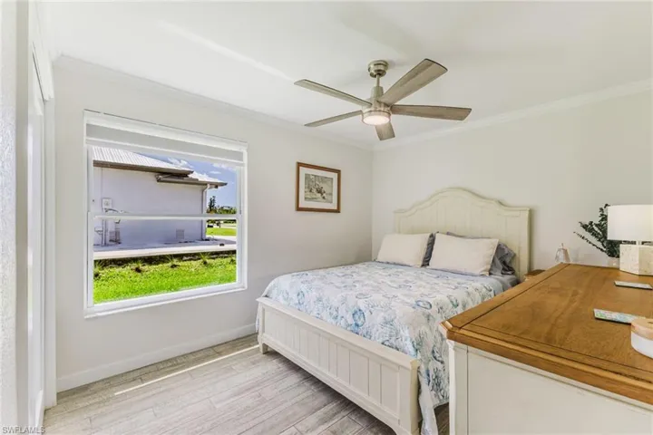 Bedroom featuring light wood-style flooring, ornamental molding, and a ceiling fan