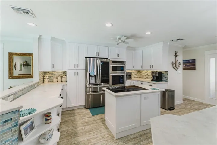 Kitchen featuring white cabinets, stainless steel appliances, crown molding, a kitchen island, and light wood-type flooring