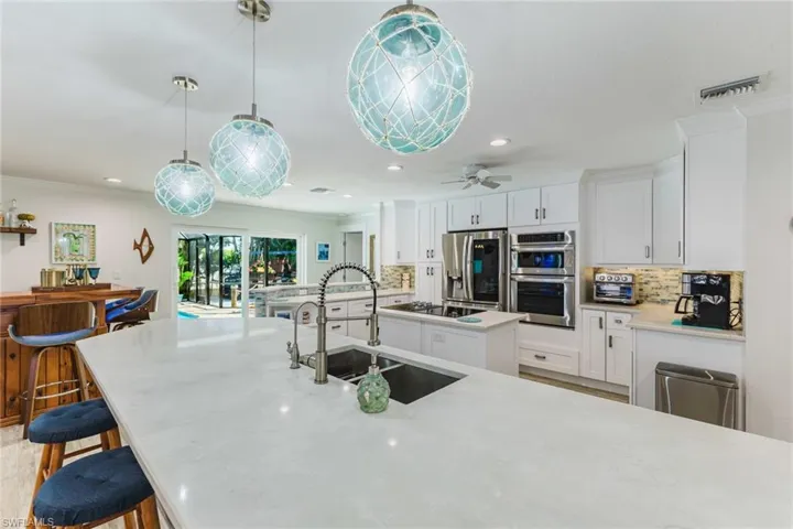 Kitchen with white cabinets, a kitchen breakfast bar, pendant lighting, stainless steel appliances, and a center island with sink