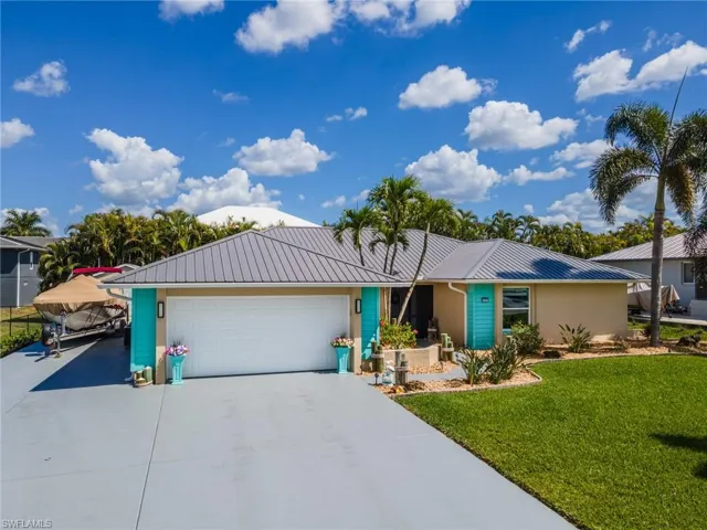 Single story home with a front yard, driveway, a garage, and a metal roof