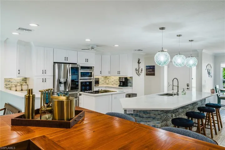 Kitchen featuring a kitchen island with sink, white cabinets, stainless steel appliances, a kitchen bar, and ornamental molding
